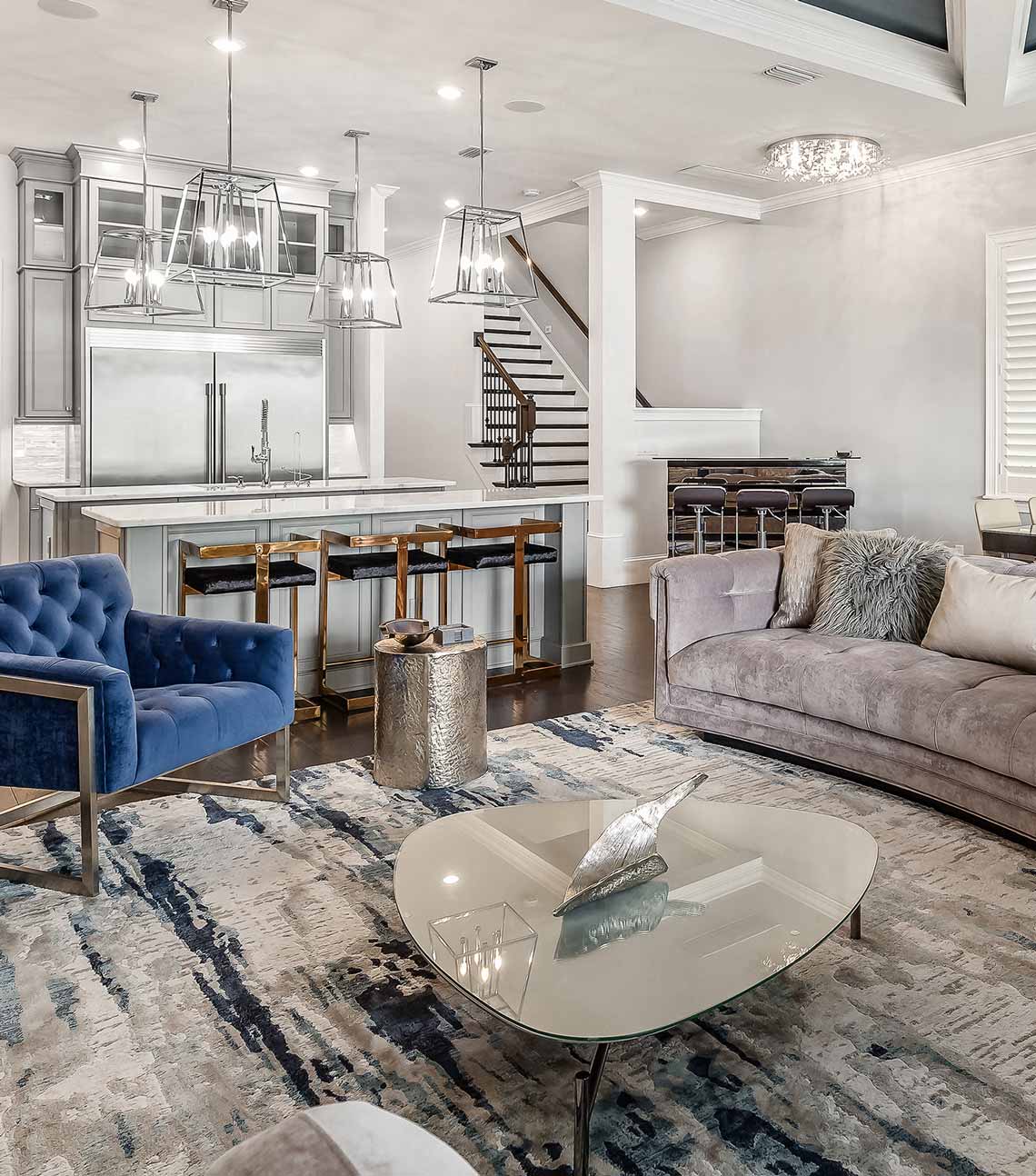 living room with silver couch and blue chair and kitchen in the background