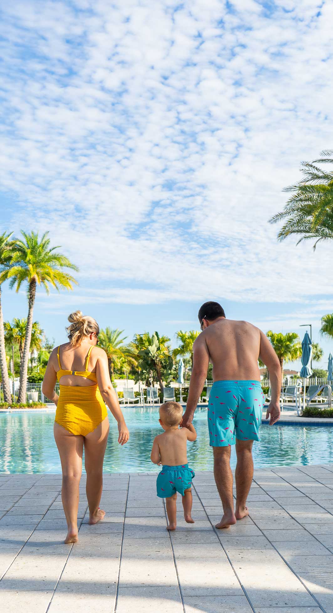couple and child holding hands walking into the pool