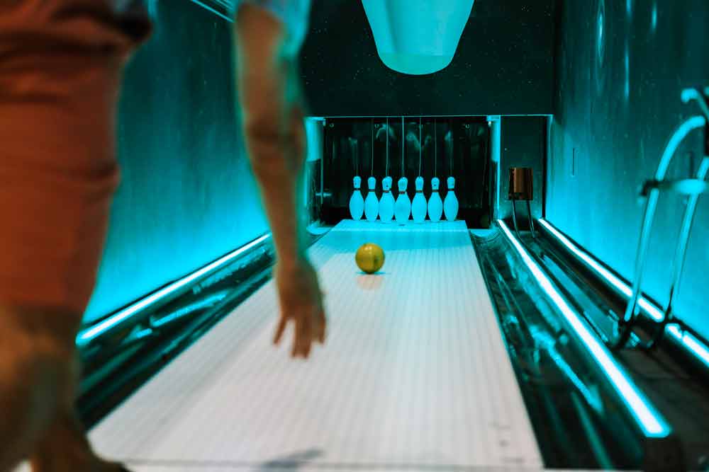 person watching a ball roll down a bowling lane towards pins